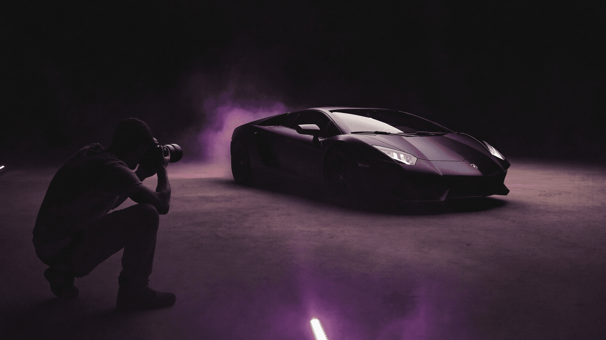 A photographer shooting a parked exotic car over the shoulder while the owner looks on